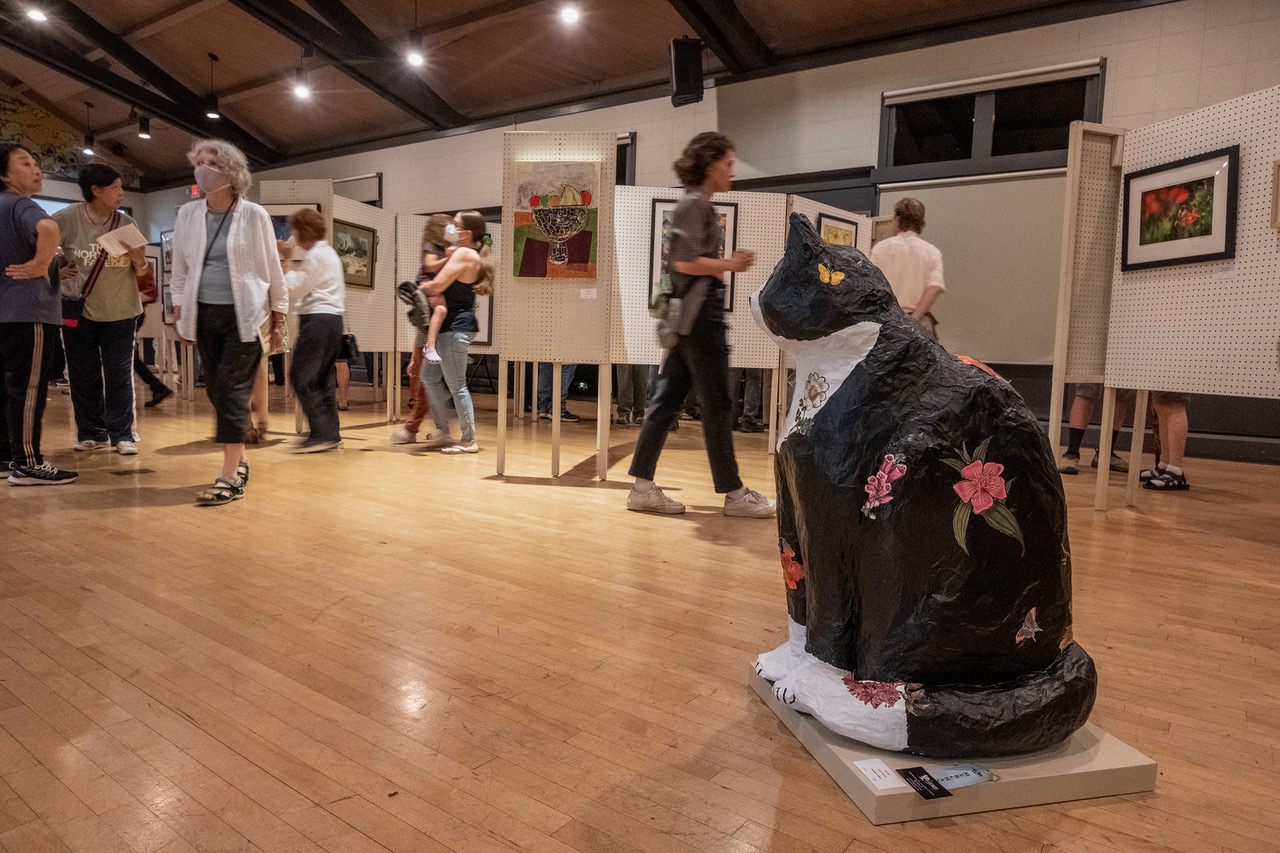 people walking in an art gallery with paper machete cat in the foreground